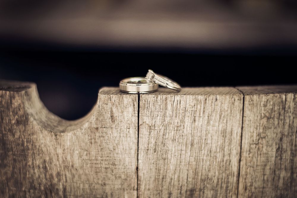 Wedding rings photographed on weathered wooden surface with dramatic lighting.