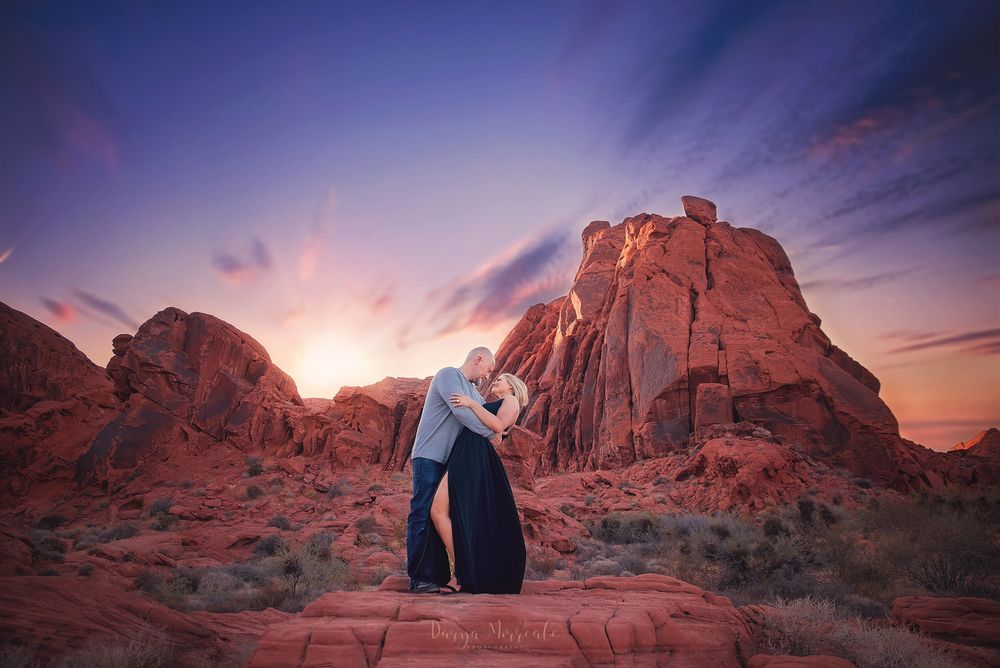 A sunset engagement photo in red rock desert landscape with dramatic pink and purple sky.