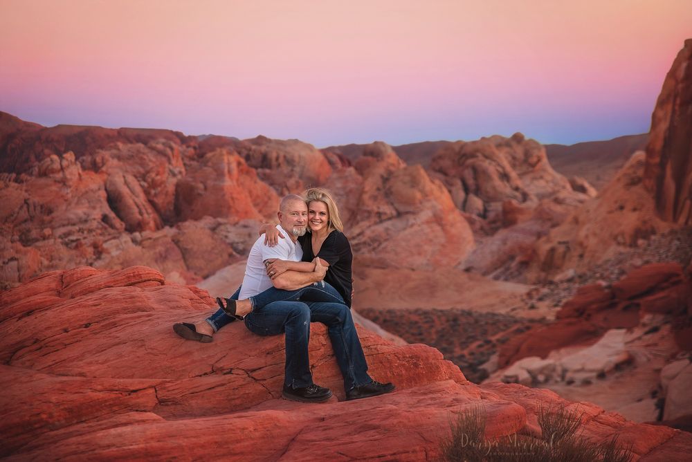 A couple enjoys sunset views while sitting on red rocks in the desert.