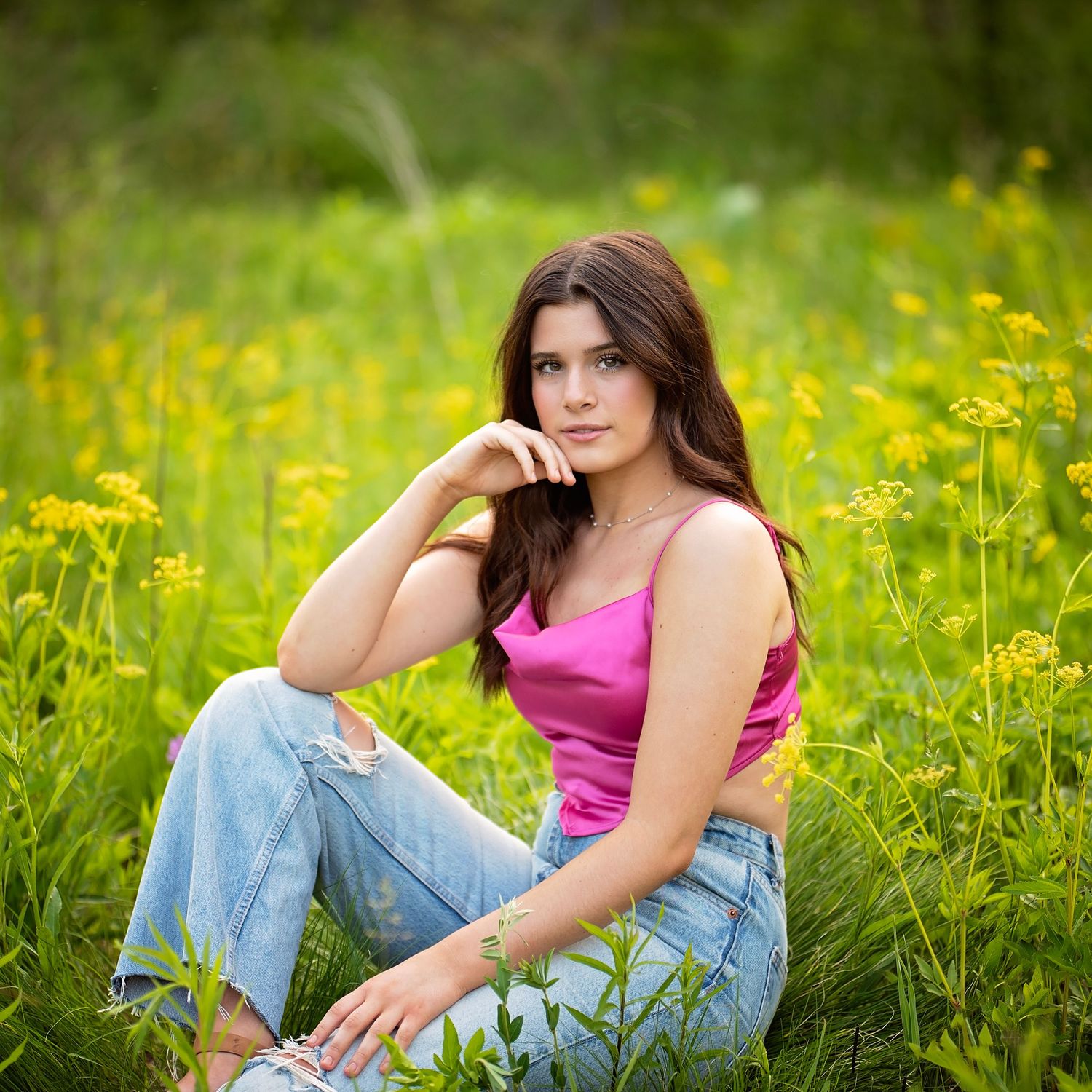 Young brunette woman in pink top and jeans sitting in a field of yellow wildflowers.