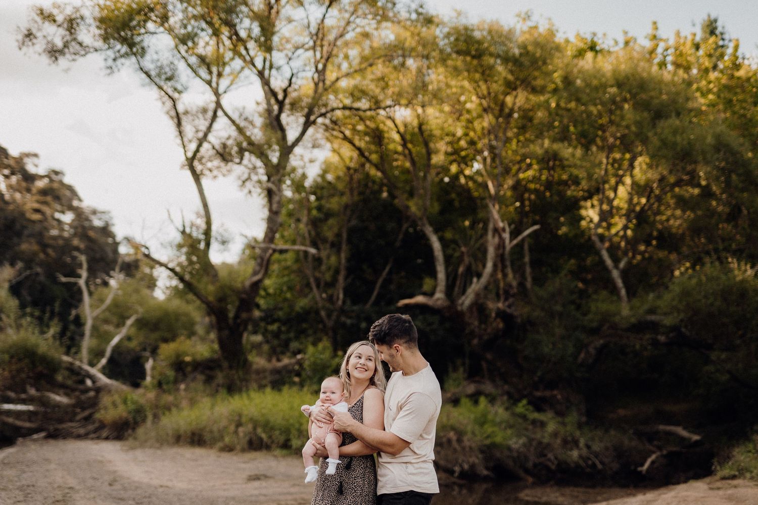 Couple embraces outdoors during golden hour photo session near trees.