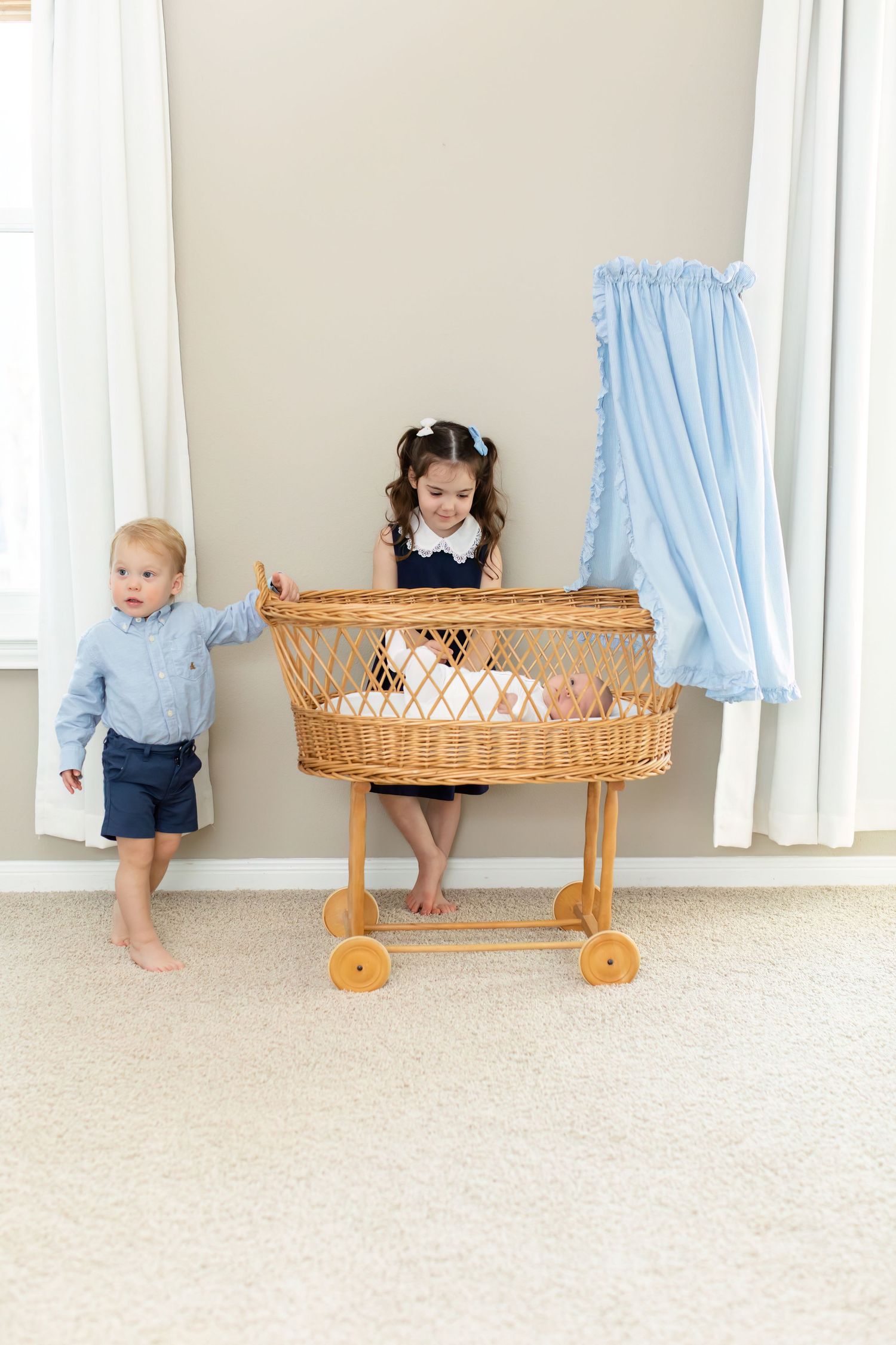 Children playing near vintage wicker baby bassinet with blue curtains.