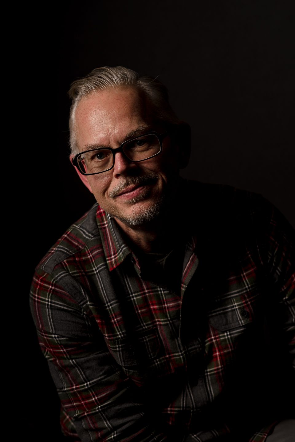 Low-key portrait of person in plaid shirt against dark background.