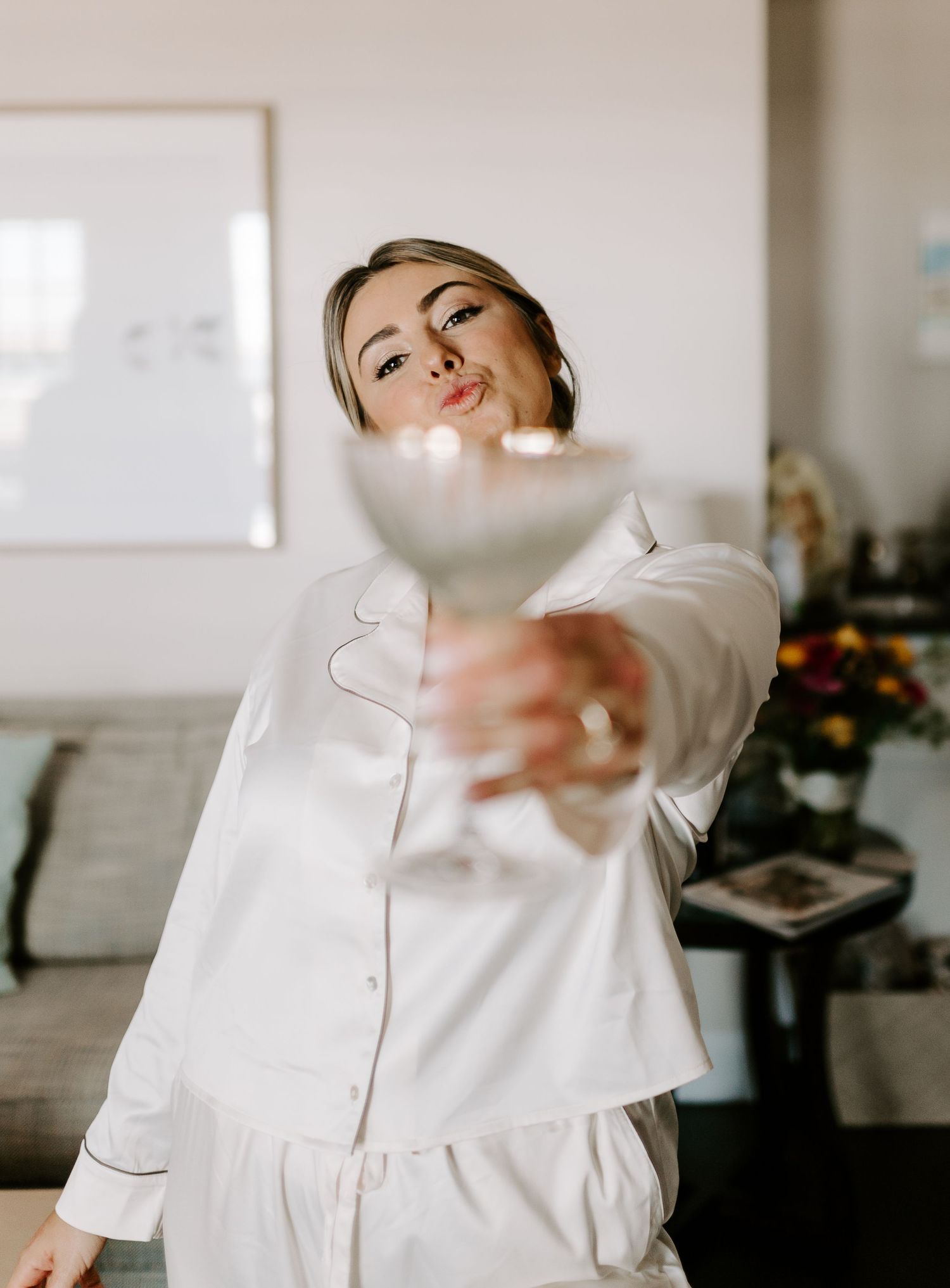 Person in white outfit playfully poses while popping champagne indoors.
