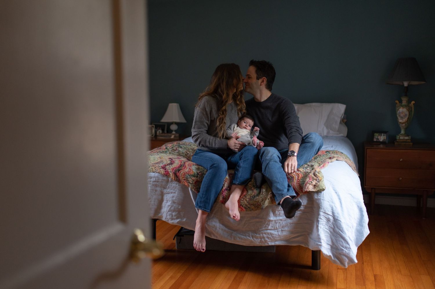 Family sitting together on a bed with their new baby in a cozy bedroom.