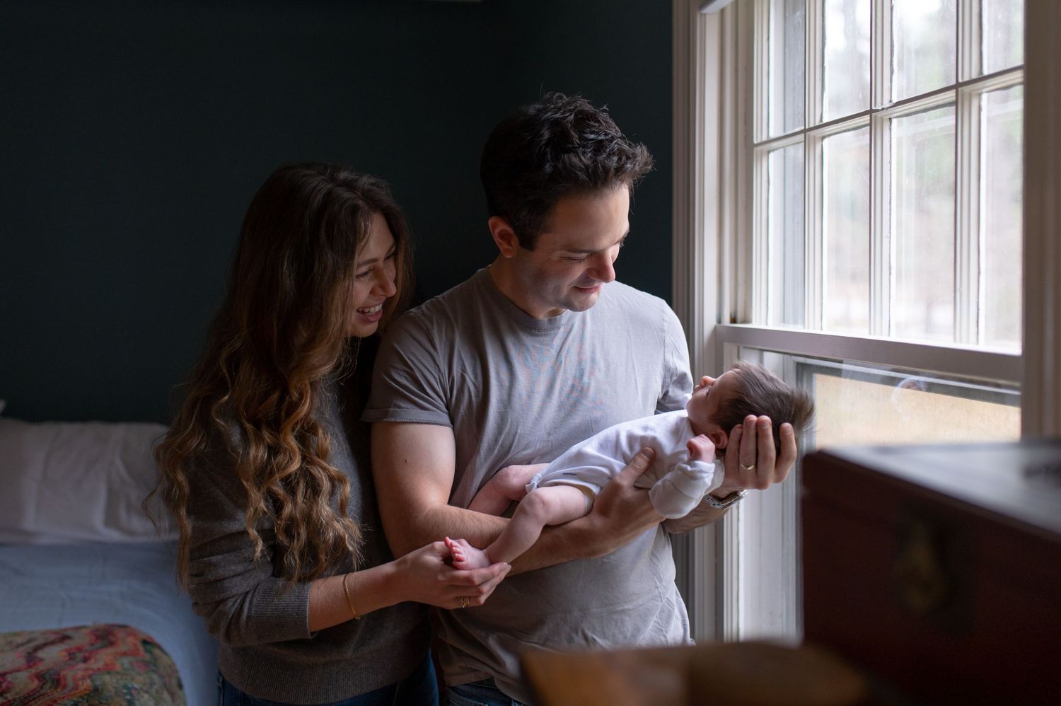 Parents tenderly holding their newborn baby by a window in soft natural light.