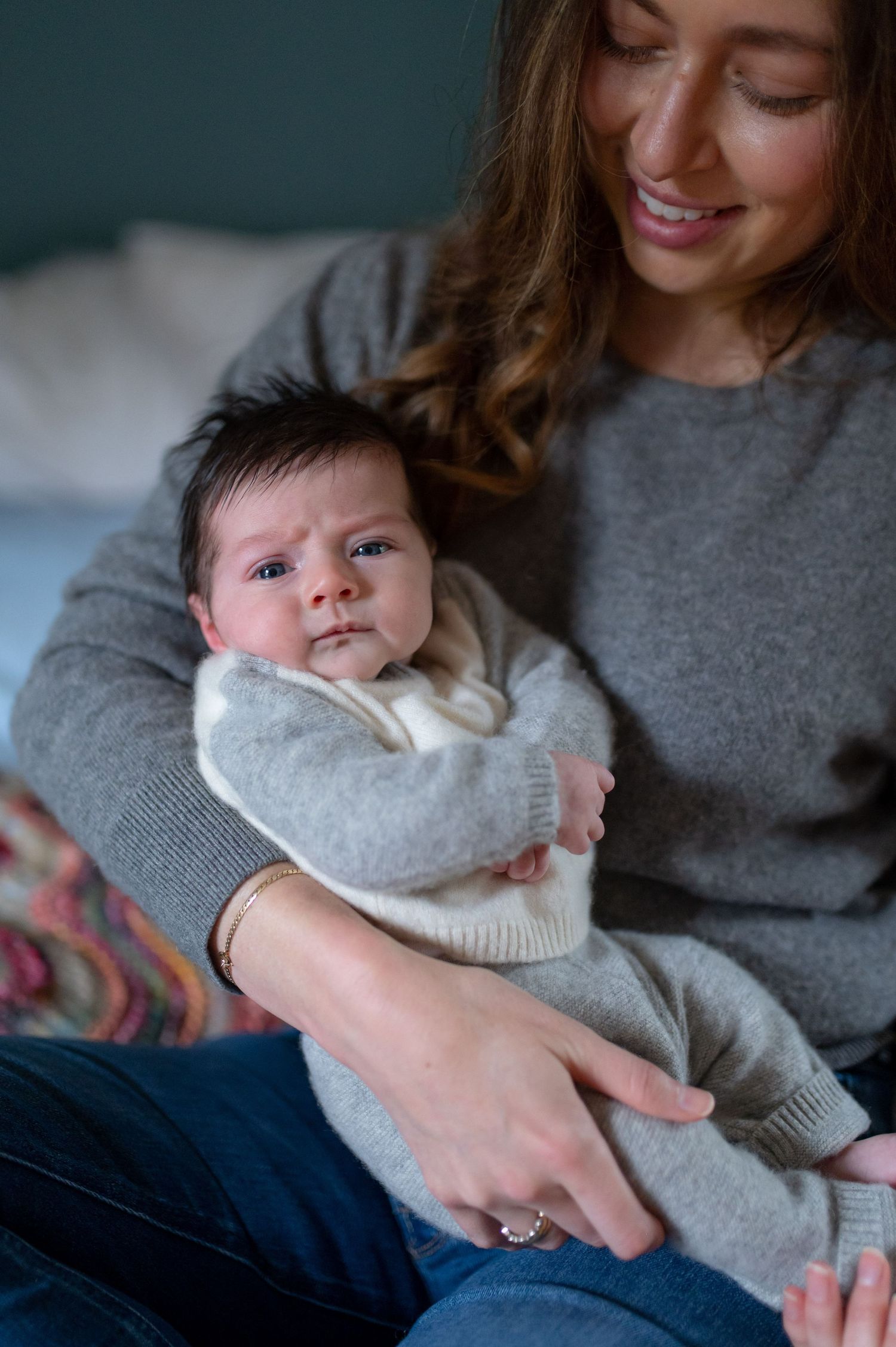 Baby in white sweater being held while looking directly at camera.