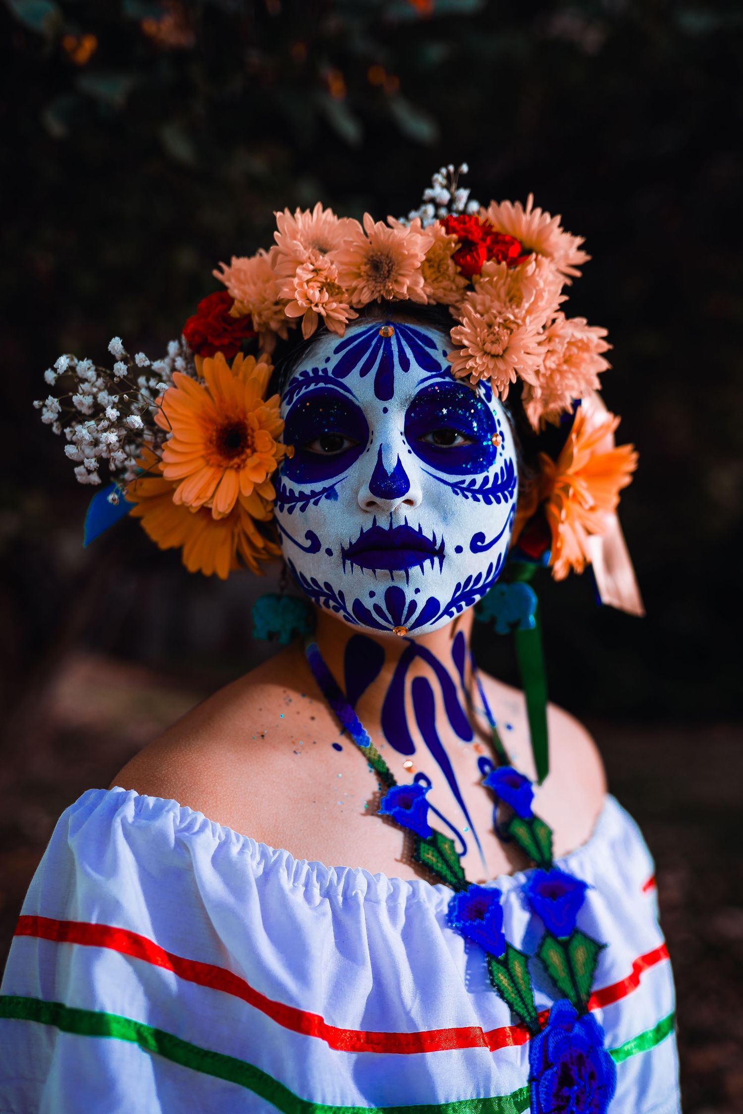 Person in Dia de los Muertos makeup wearing a blue skull mask and floral crown.