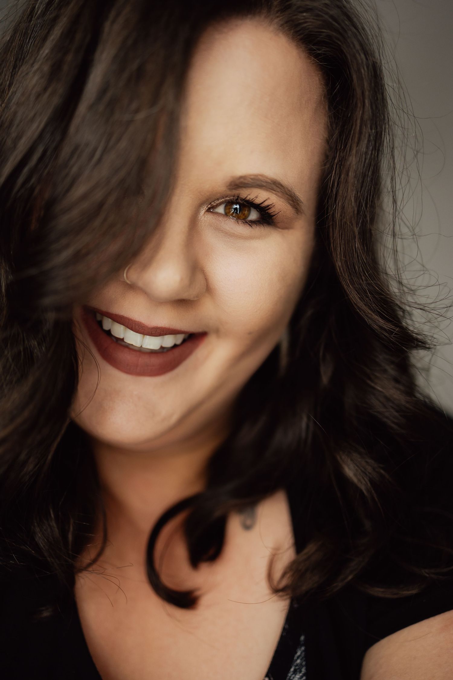 Close-up portrait showing dark hair and bright smile against neutral background.