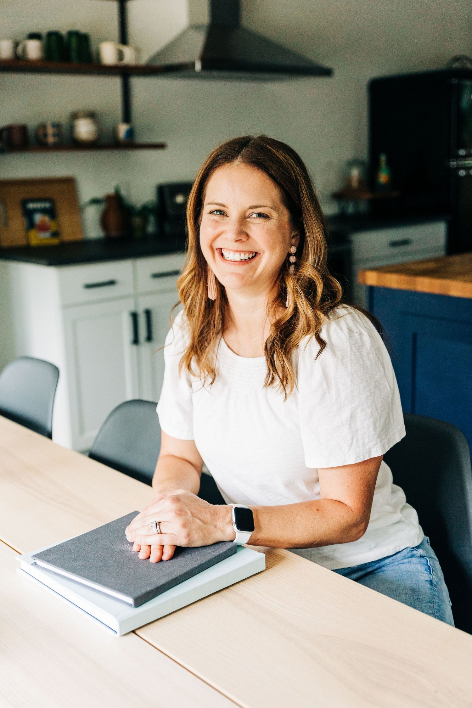 woman poses for personal brand photography sitting at table with hands on top of photo albums