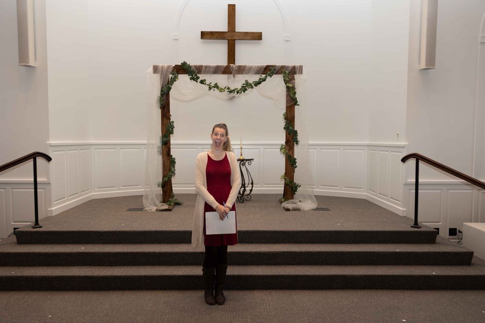 Wooden cross and floral arch frame altar area in simple church interior.
