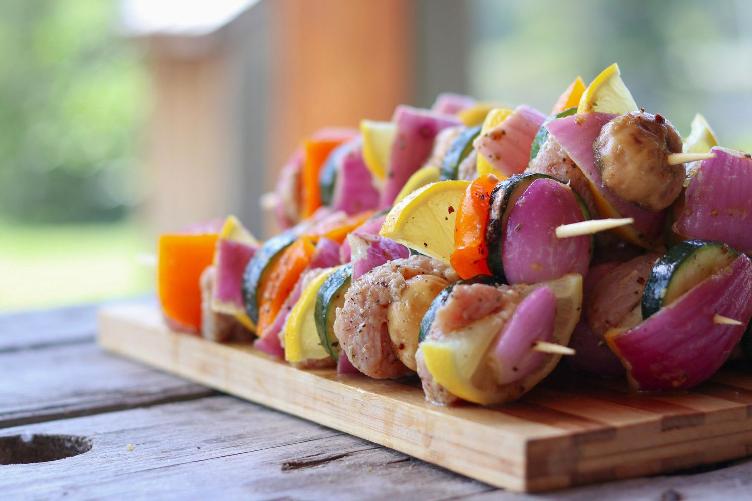 Colorful grilled vegetable and meat kabobs arranged on wooden cutting board.