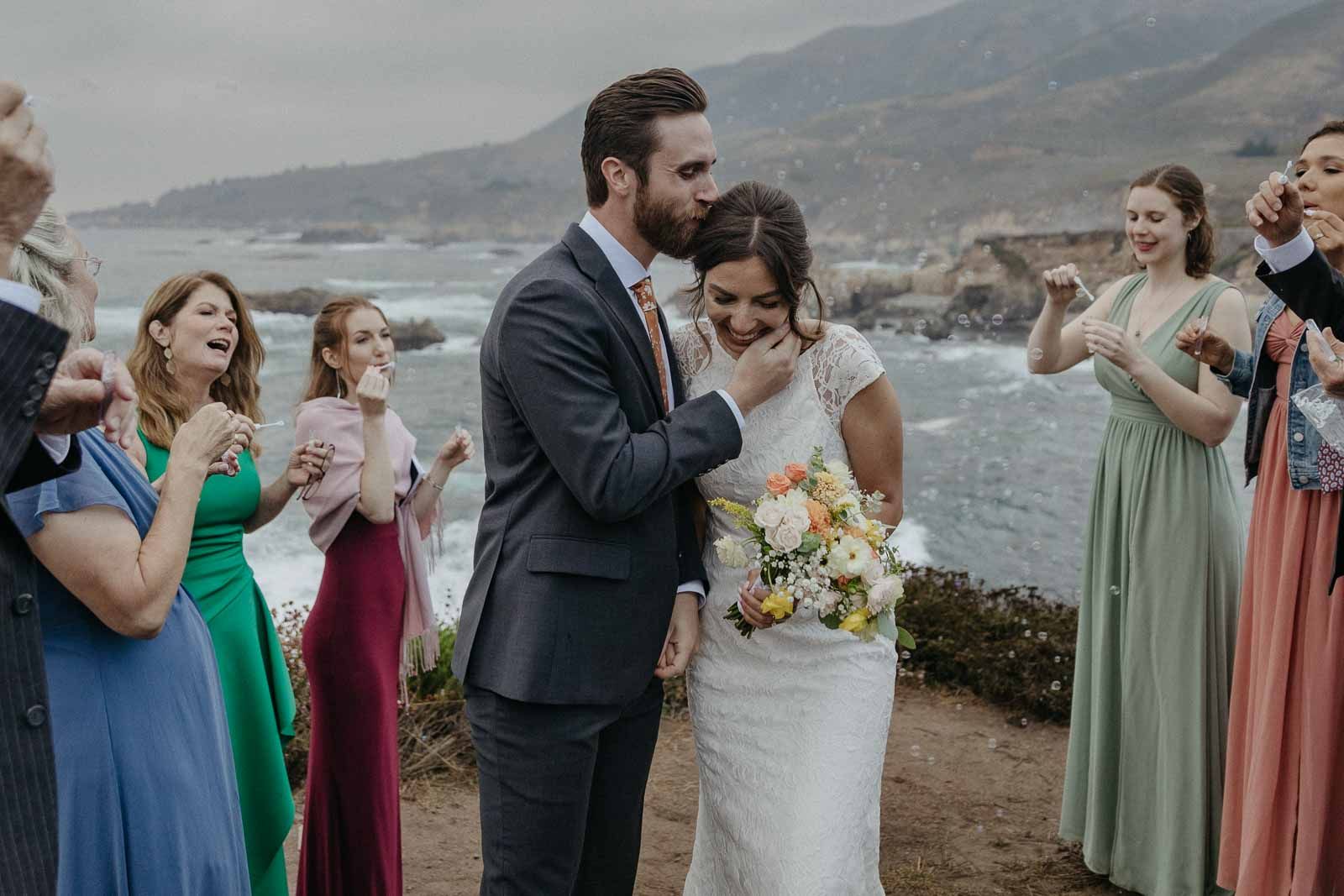 A wedding party celebrates on a scenic coastal cliff overlooking the ocean.