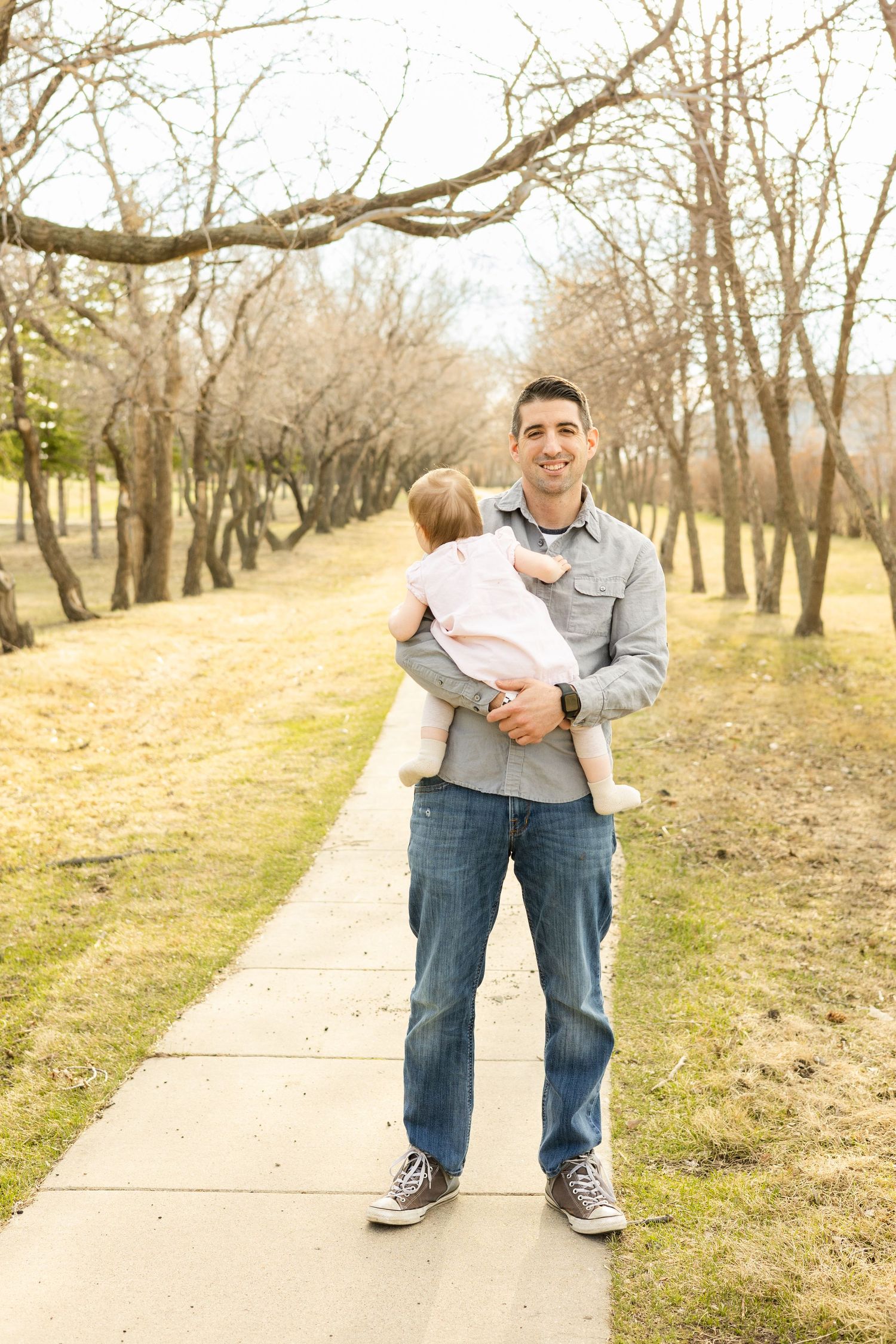 A scenic pathway through bare trees in early spring with a parent and child enjoying a walk outdoors.