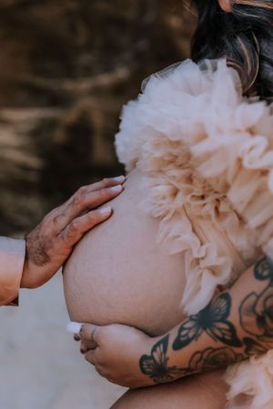 Artistic close-up of hands cradling a pregnant belly with a peach-colored robe.