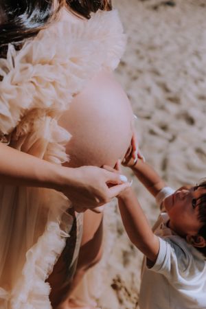 Close-up details of delicate white maternity dress fabric against sandy beach.