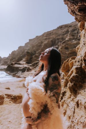 Dramatic maternity photo against coastal cliffs and ocean backdrop.