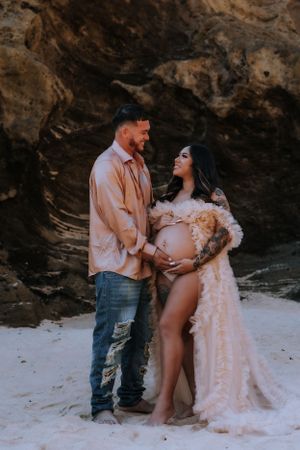 Intimate maternity photos captured on a sandy beach with dramatic rock formations in the background.