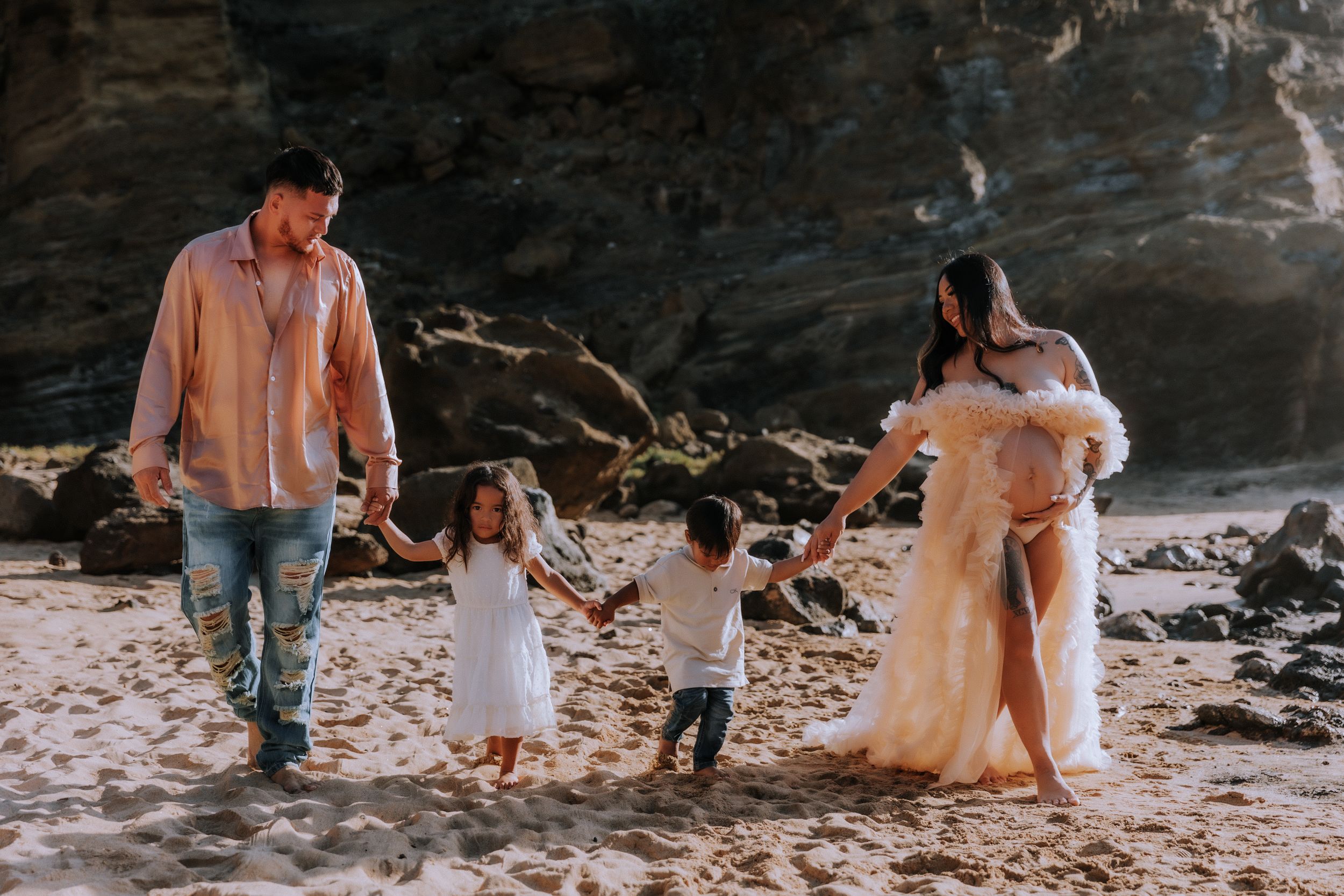Family group relaxing together on rocky beach at sunset.