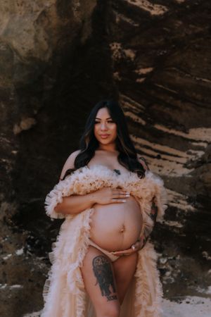 Maternity photoshoot featuring a flowy peach-colored robe against a rocky backdrop.
