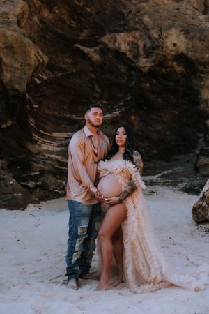 Couple in romantic photoshoot against rocky beach backdrop.