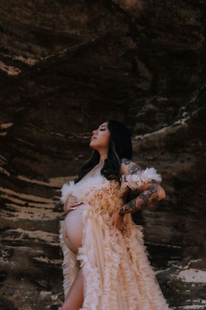 Artistic maternity portrait with a flowing dress against textured rock formations.