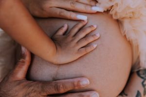 Black and white close-up of hands tenderly holding a pregnant belly.