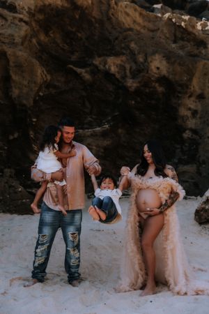 Family maternity photo session on a beach with rocky cliffs in the background.