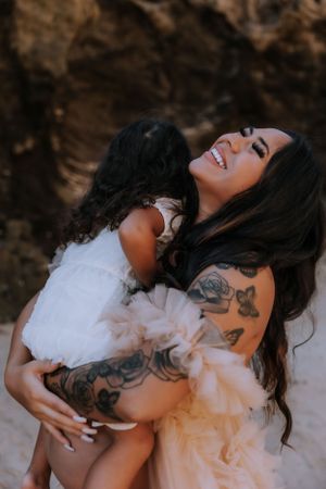 Joyful maternity portrait with white flowy dress against rocky backdrop.