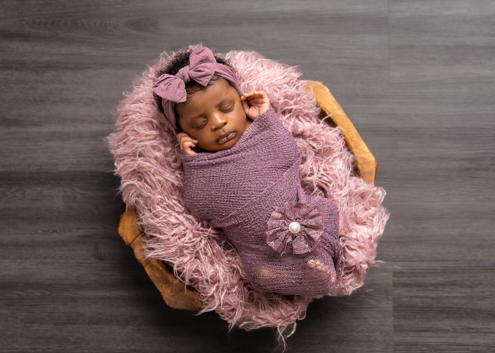 Newborn baby sleeping peacefully wrapped in purple fabric with floral details.