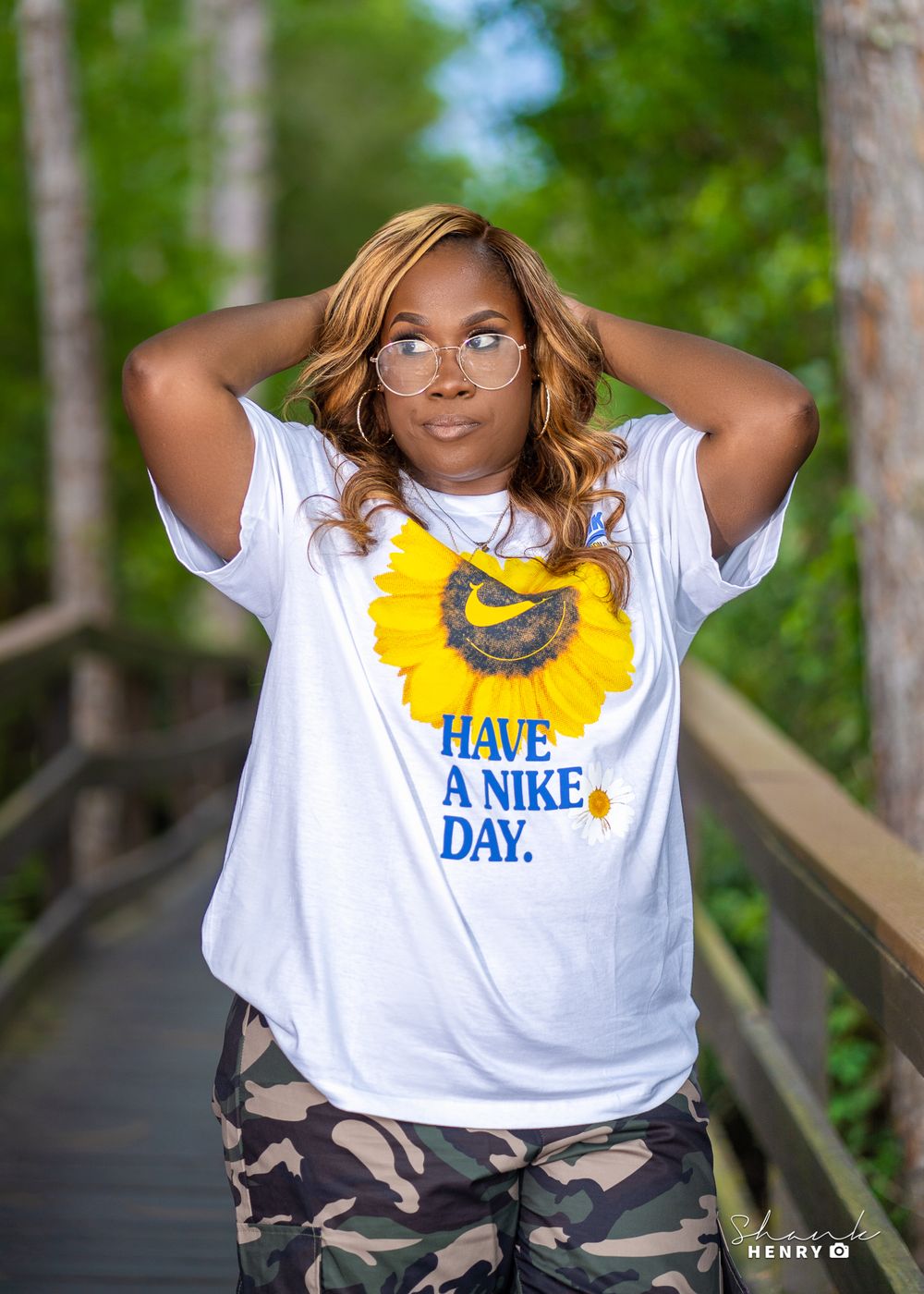 Outdoor portrait on a wooden bridge wearing a graphic t-shirt with sunflower design and camo pants.