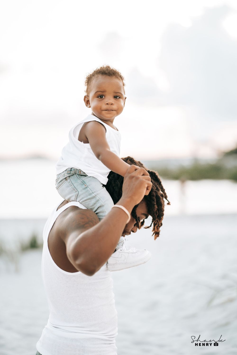Parent lifting child joyfully against bright white sky at beach.