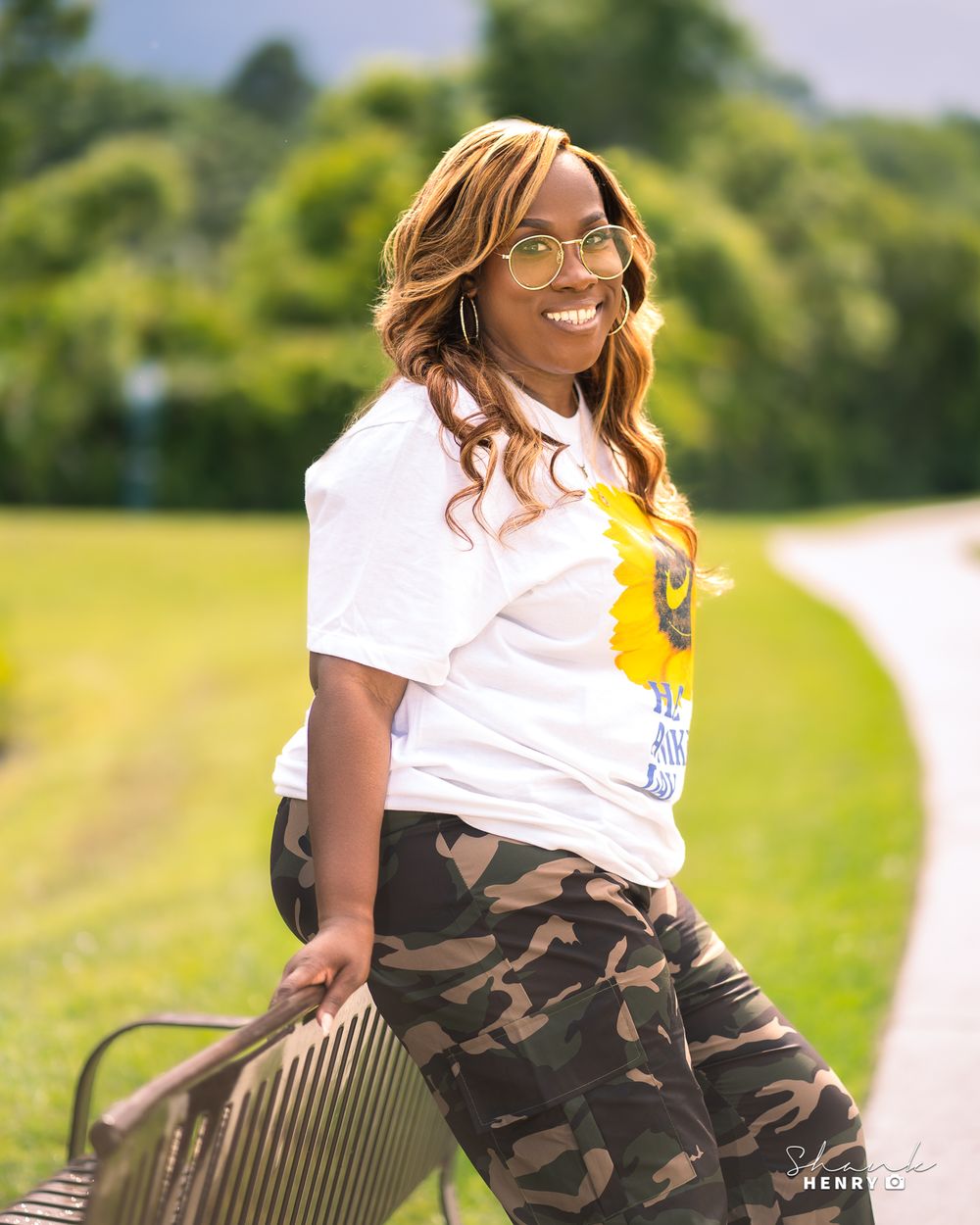 Casual outdoor portrait featuring someone in a white t-shirt and camo pants with a handbag.