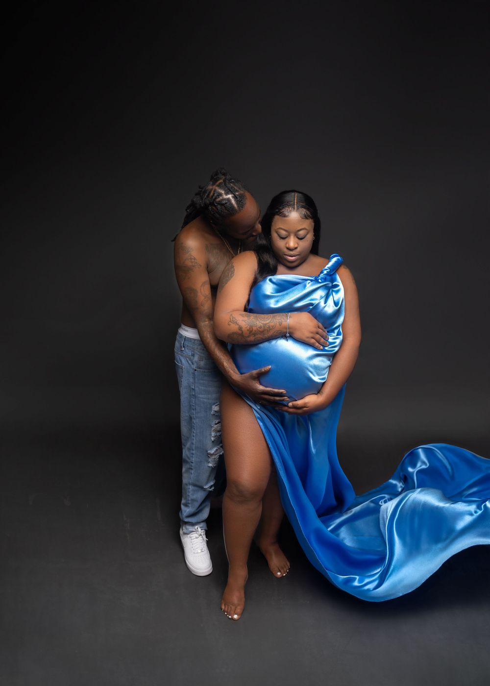 Artistic maternity photo with flowing blue silk fabric against dark background.