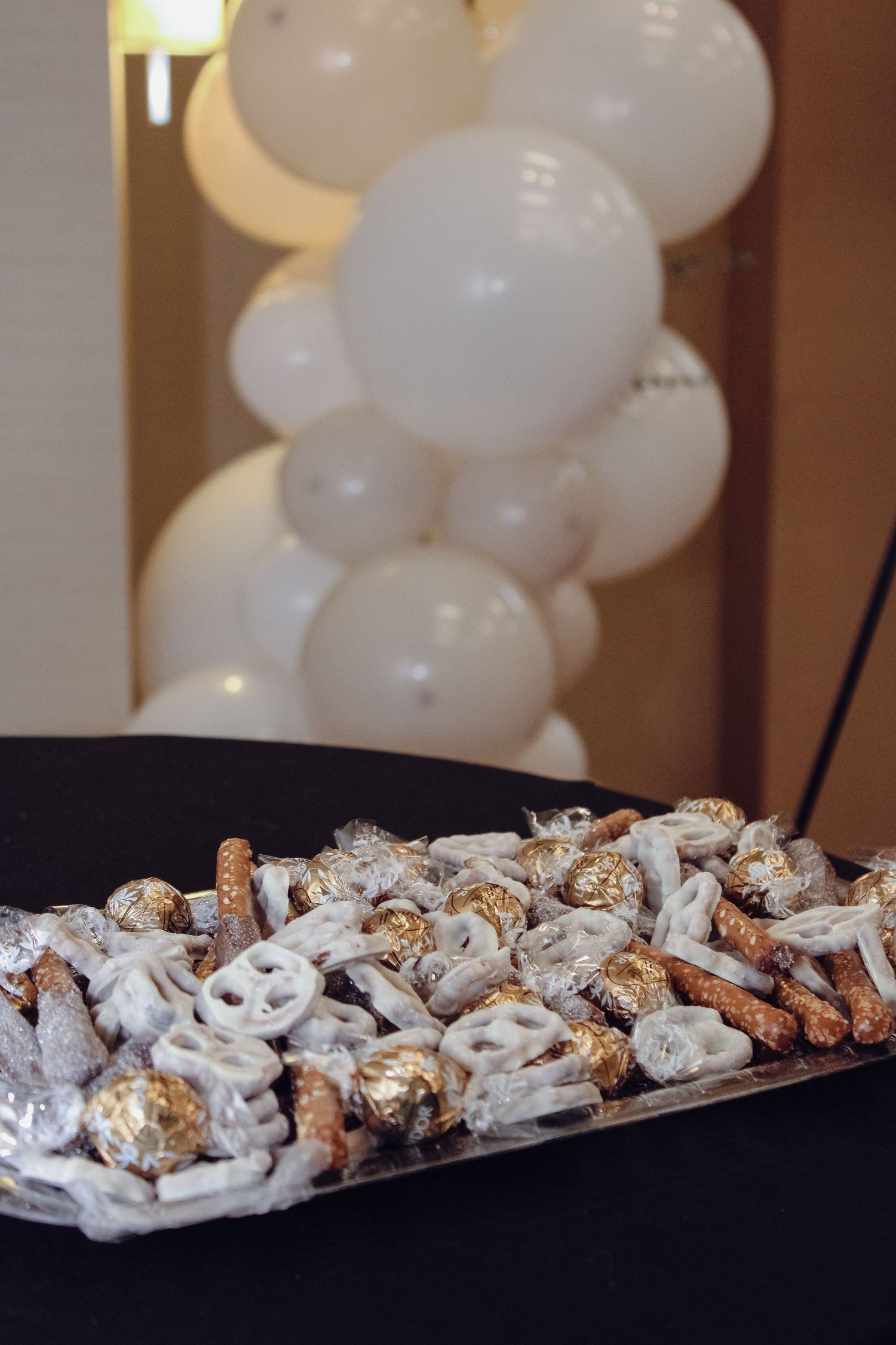 A platter of white chocolate covered pretzels and snacks displayed with balloon decor.