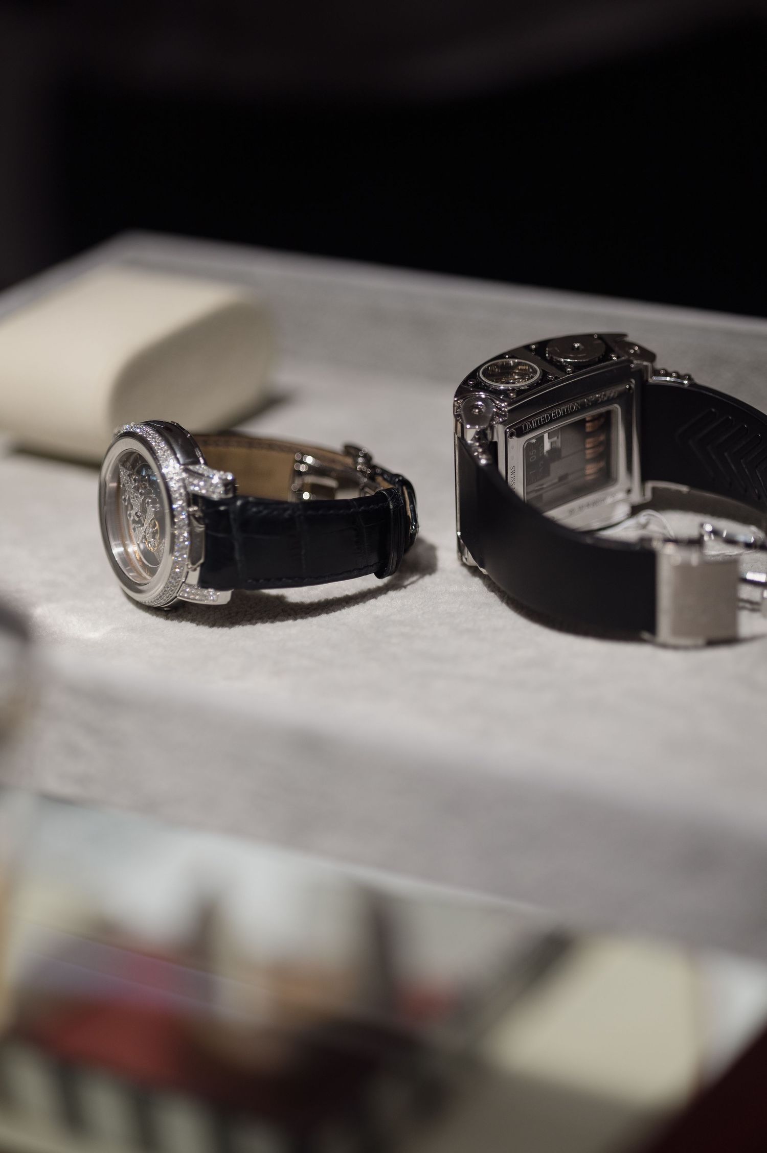 Two luxury watches with black leather straps displayed on light surface.