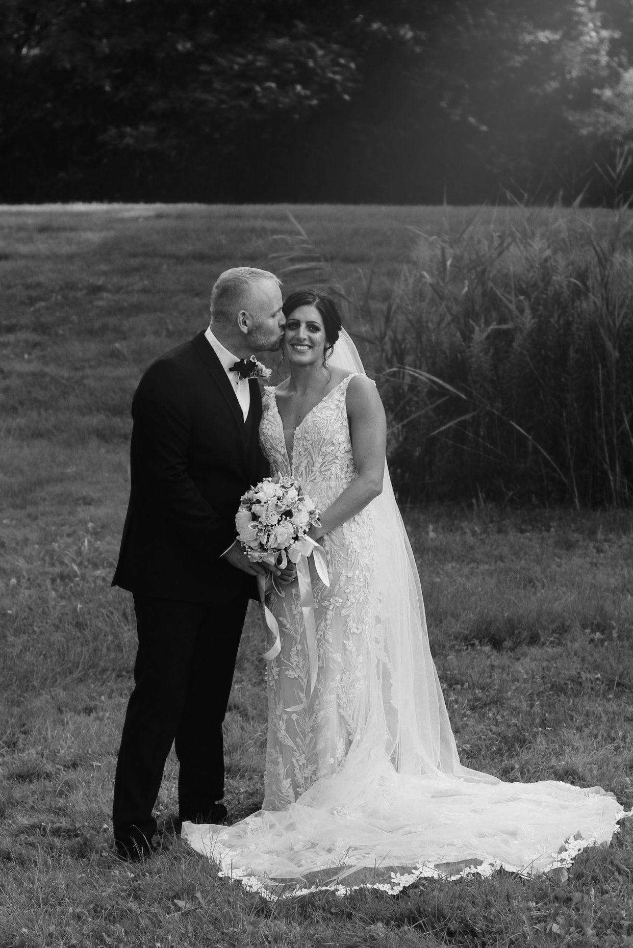 Black and white wedding portrait in rustic outdoor setting.