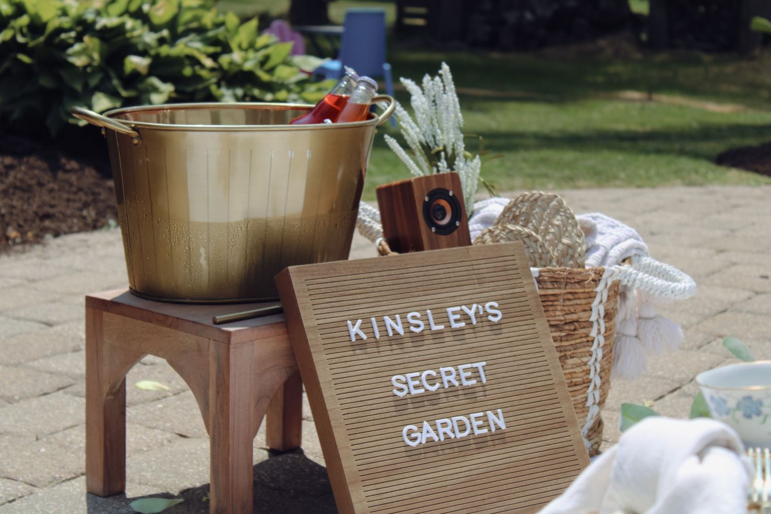 A rustic wooden sign reading 'Kinsley's Secret Garden' next to a gold bucket outdoors.