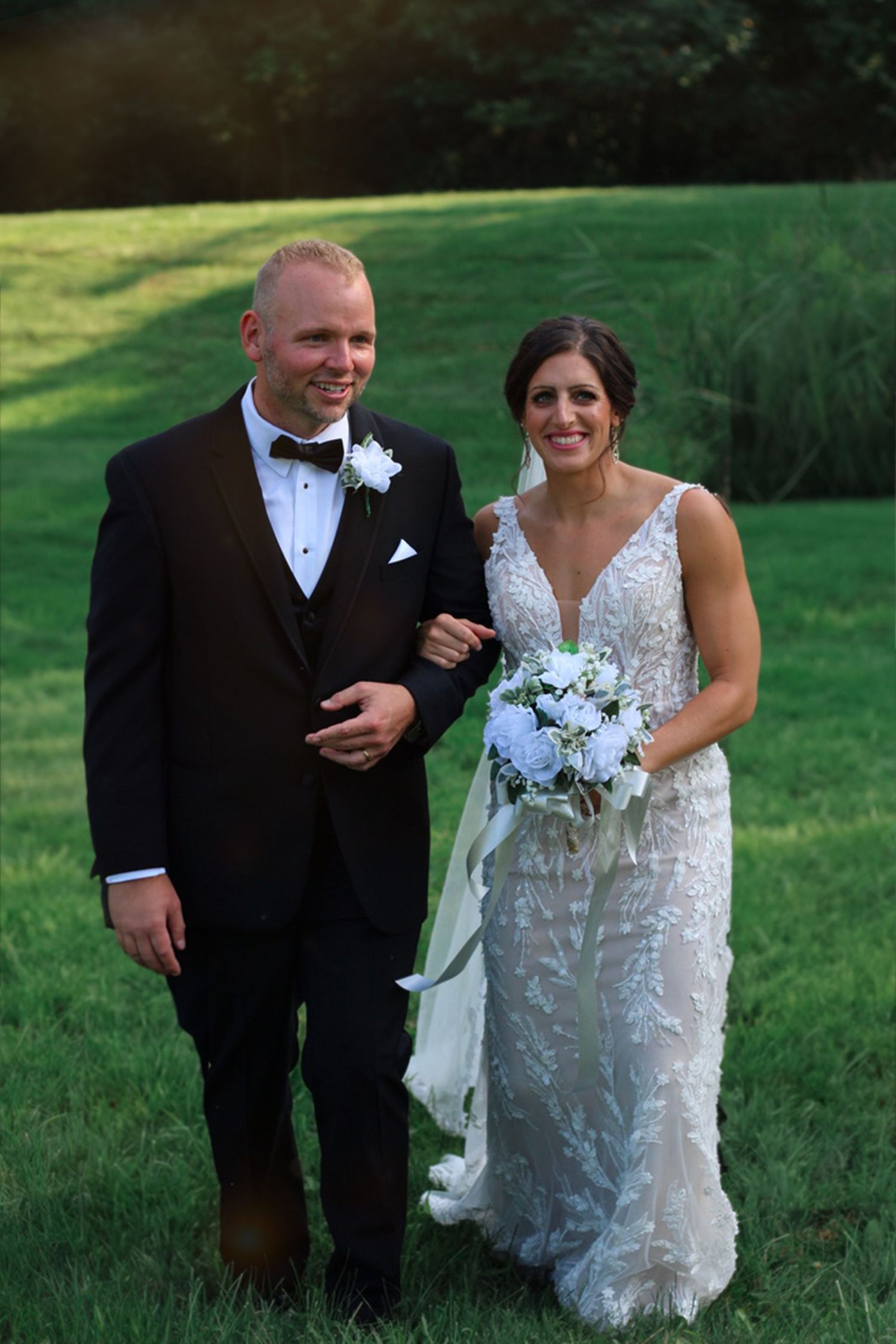 Happy couple poses with bouquet during outdoor wedding photoshoot.