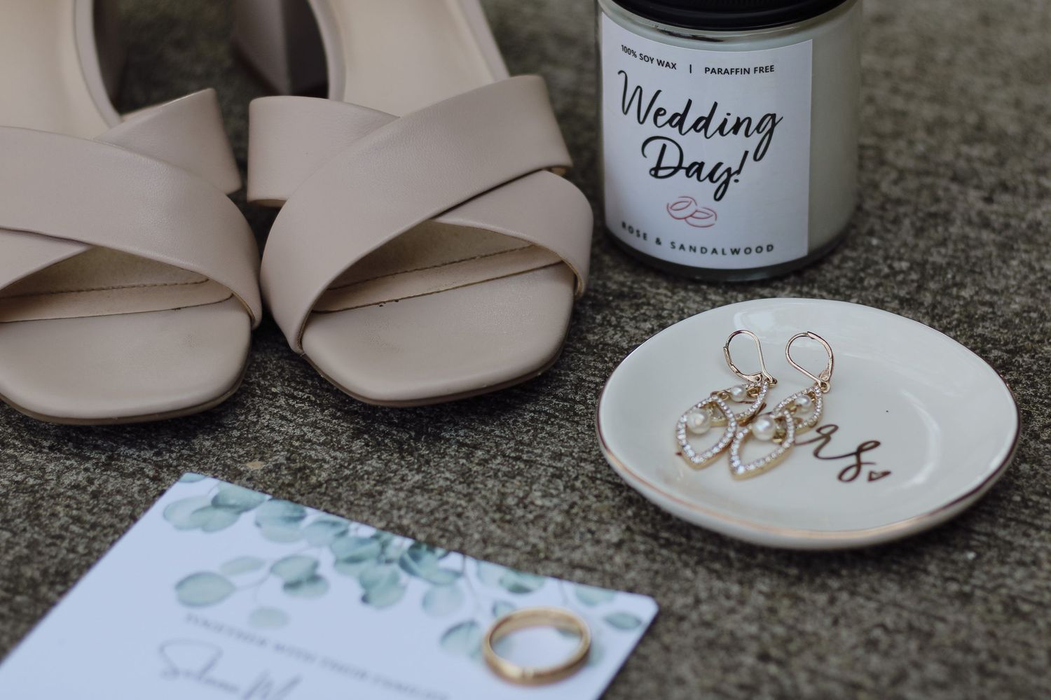 Wedding day details with bridal shoes, rings, and decorative plate on gray surface.