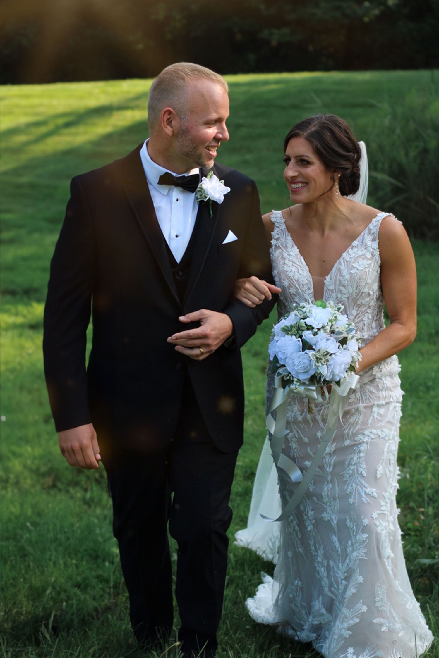 Newlywed couple walking and smiling together on a sunny lawn.