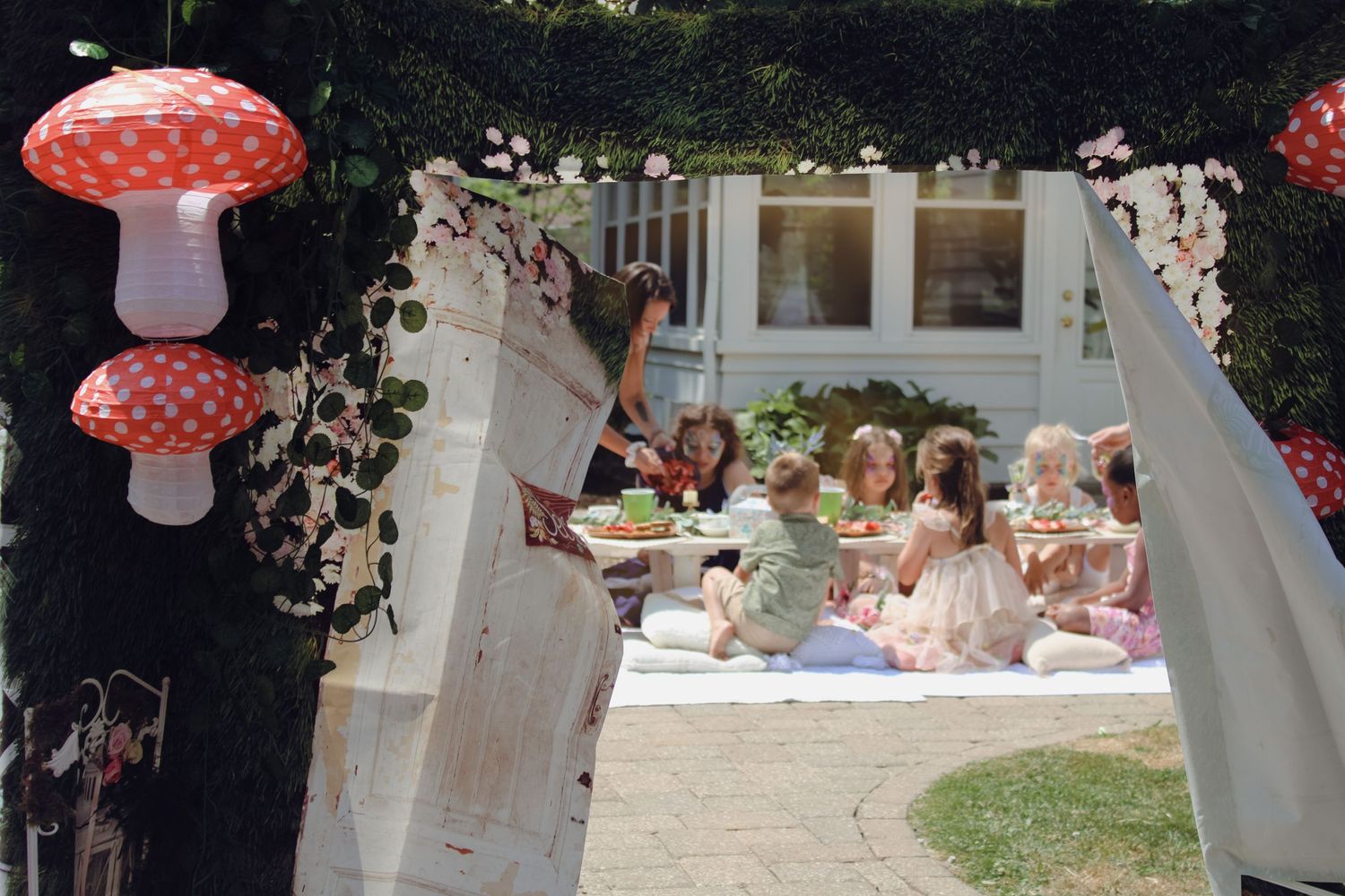 Children enjoying a whimsical garden tea party under red mushroom decorations.