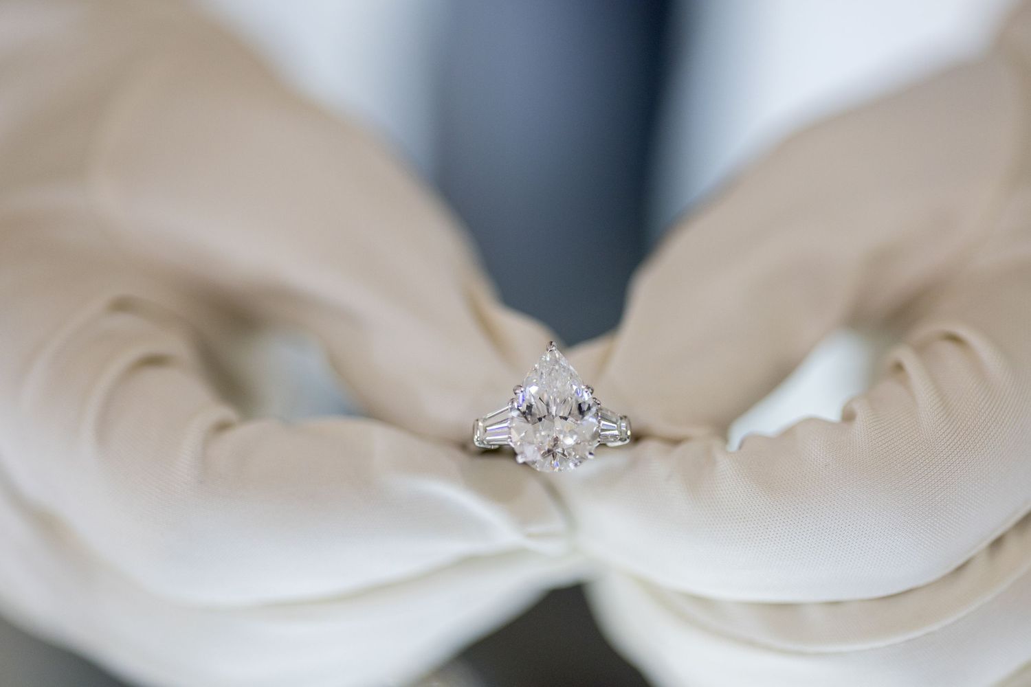 Close-up of diamond engagement ring held delicately with white gloved hands.