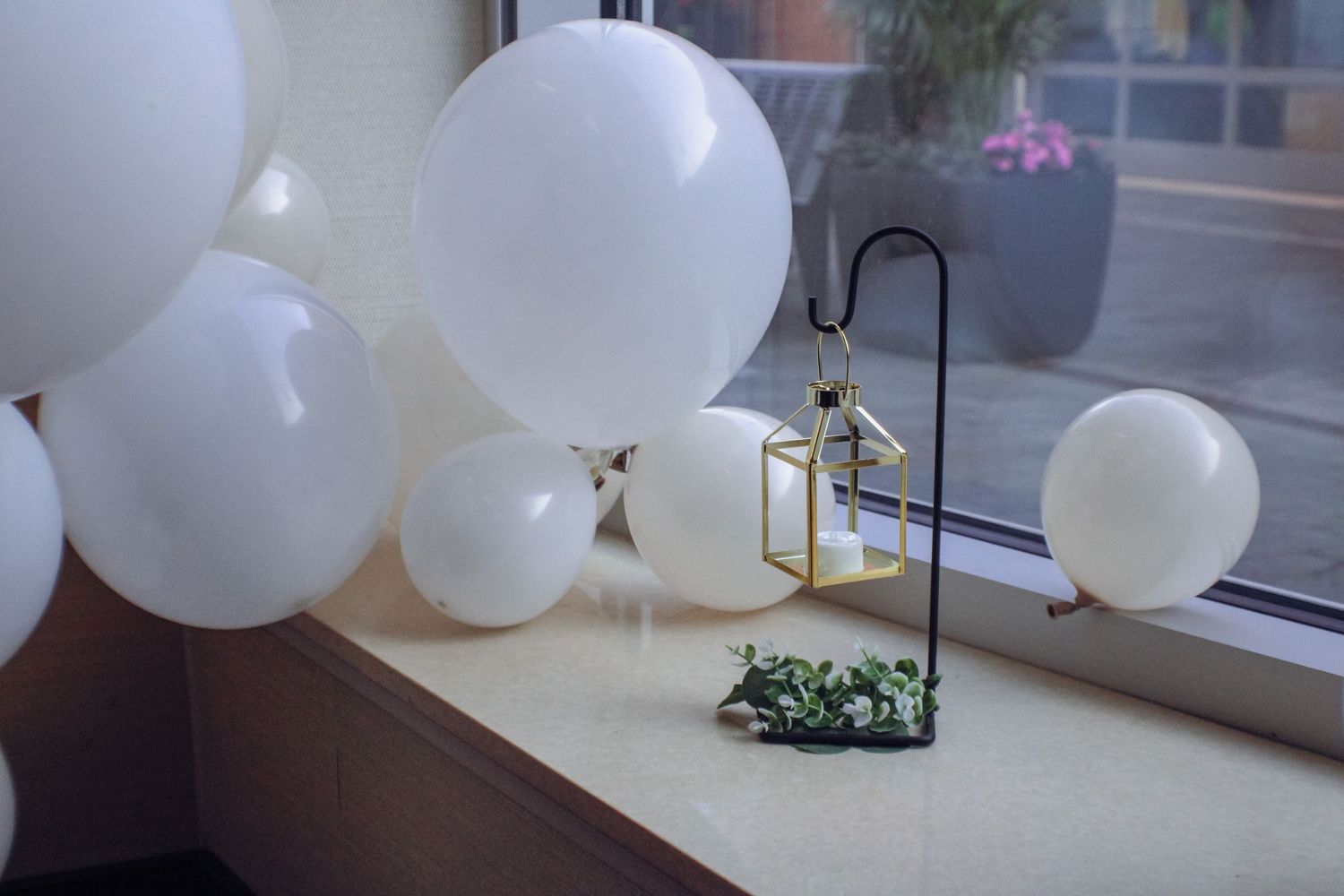 Small decorative lantern and greenery displayed on windowsill with white balloons floating around.