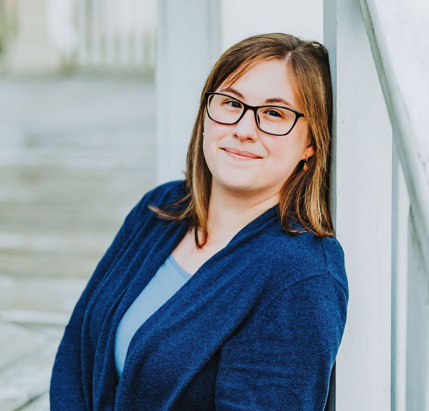 Professional headshot of someone in a navy cardigan and glasses against a light background.