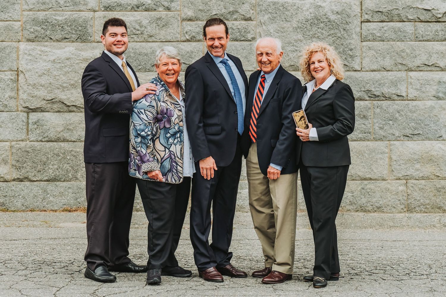 Professional group photo of business team standing against a stone wall background.