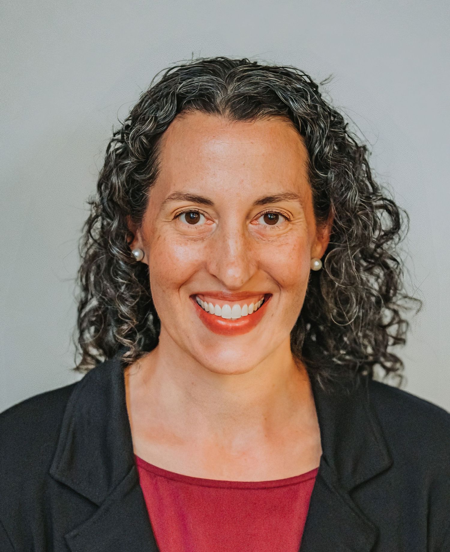 Professional portrait featuring a bright smile and curly hair against neutral background.