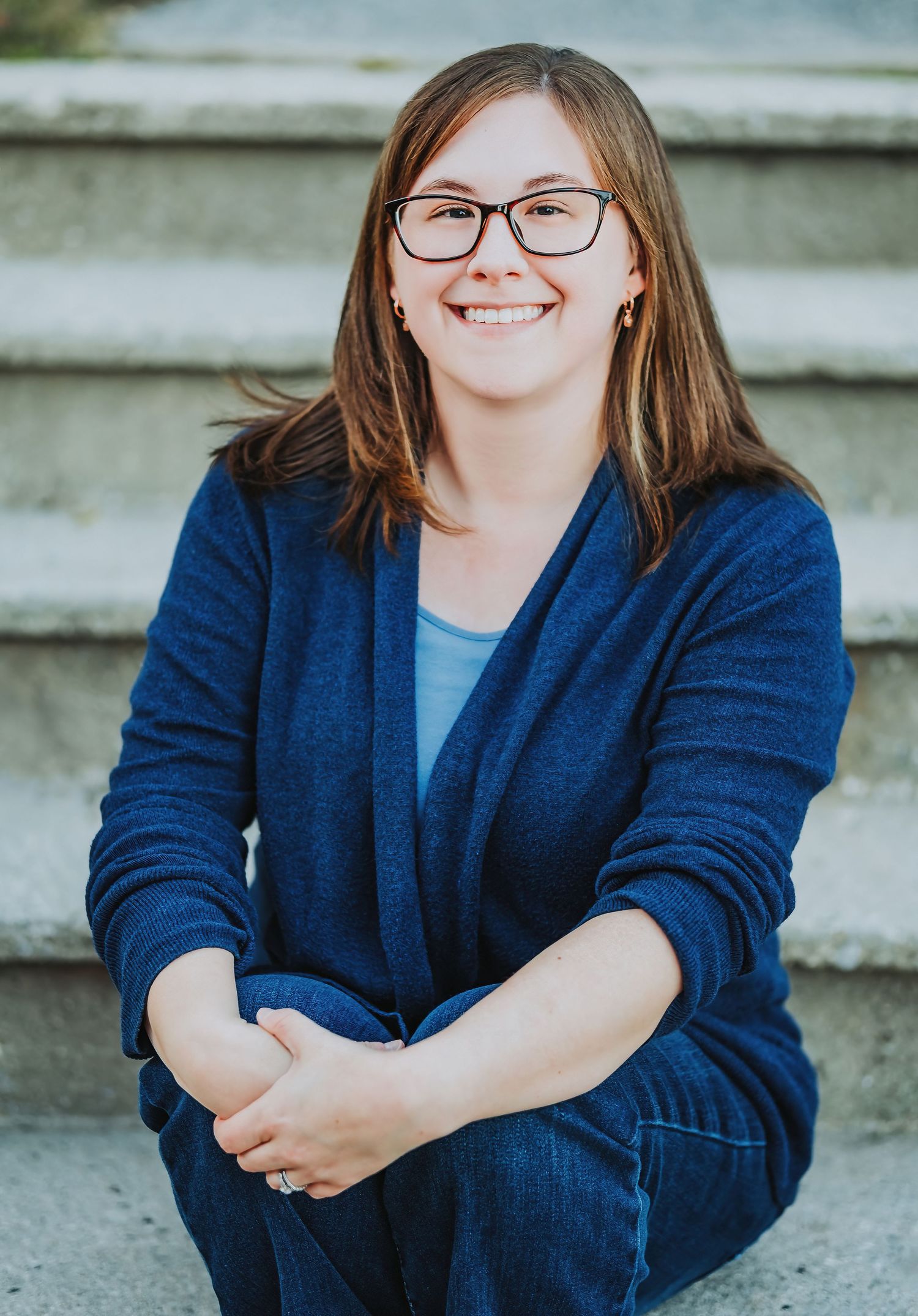 Relaxed portrait of someone in business casual attire sitting on concrete steps.
