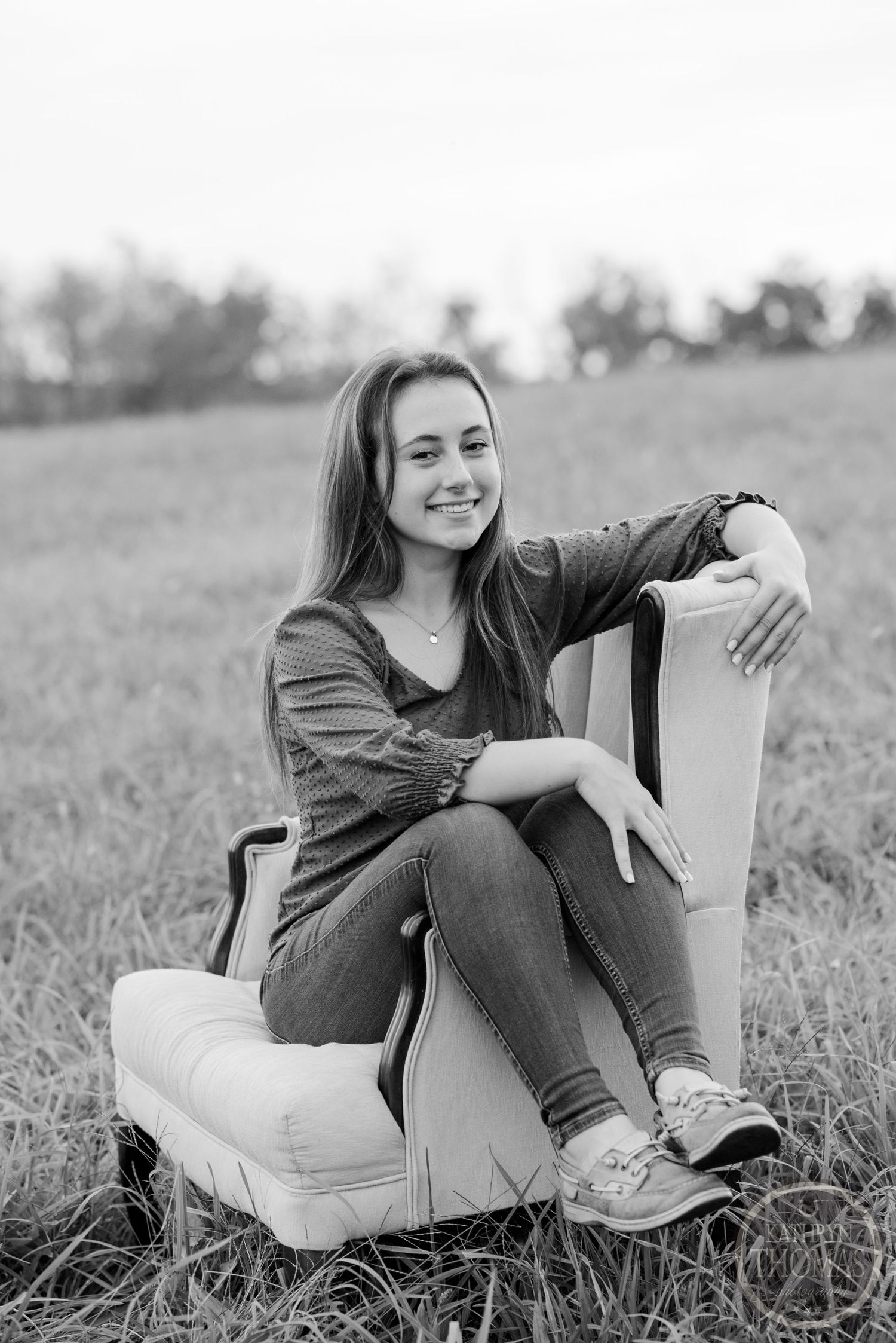 Black and white portrait of someone relaxing in a plush armchair outdoors in a field.