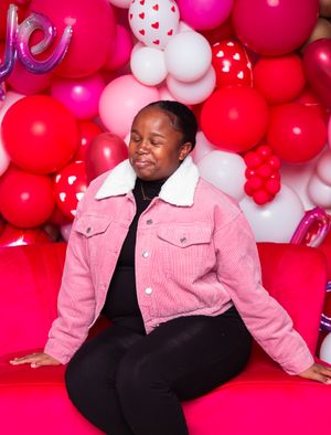 Valentine's themed photo session with pink jacket against red and white balloon backdrop.